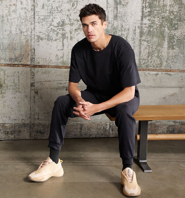 Male model sitting on a bench with black Russell Athletic tee.  