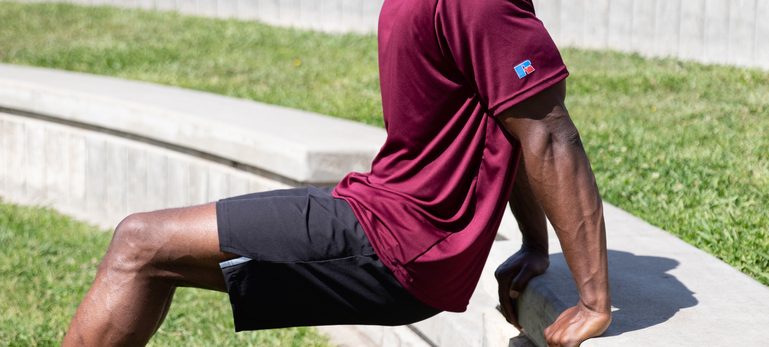 Male model wearing maroon dri-power performance t-shirt and black legend shorts outside exercising. Male model wearing maroon dri-power performance t-shirt and black legend shorts outside exercising.