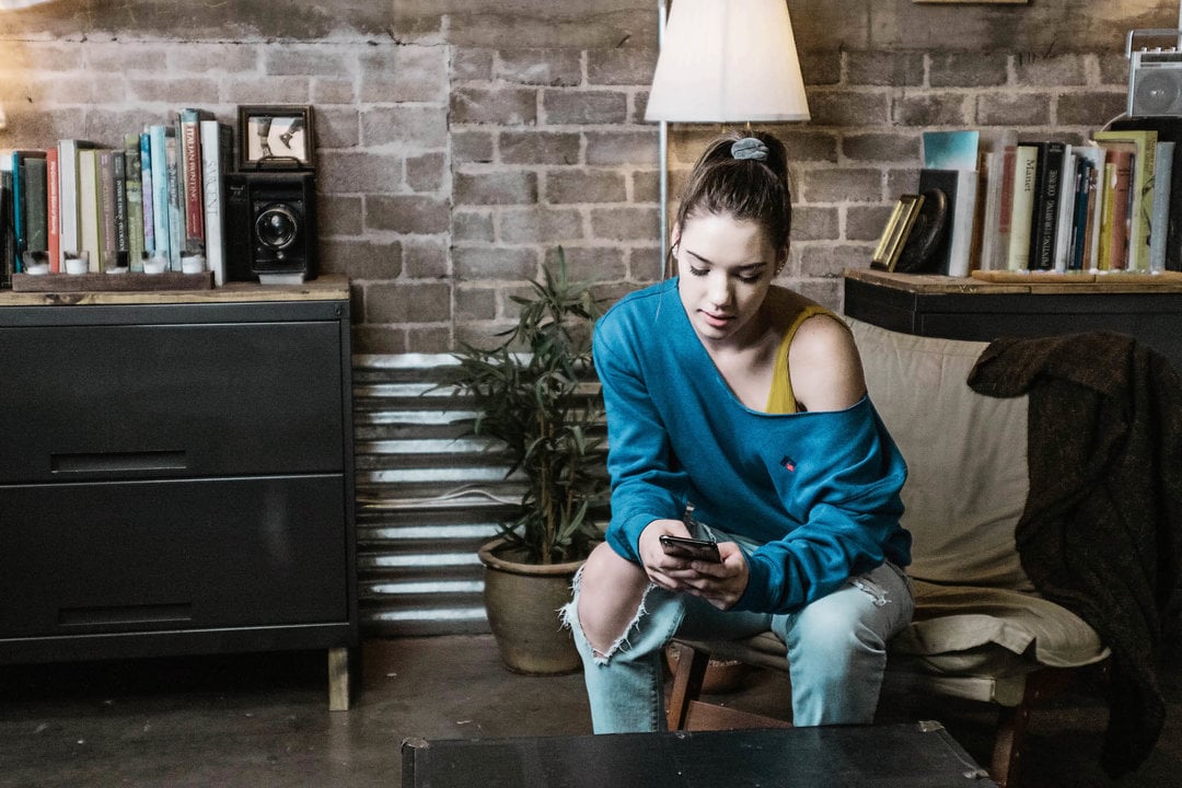 Woman in a Russell Athletic sweatshirt looking at her phone.