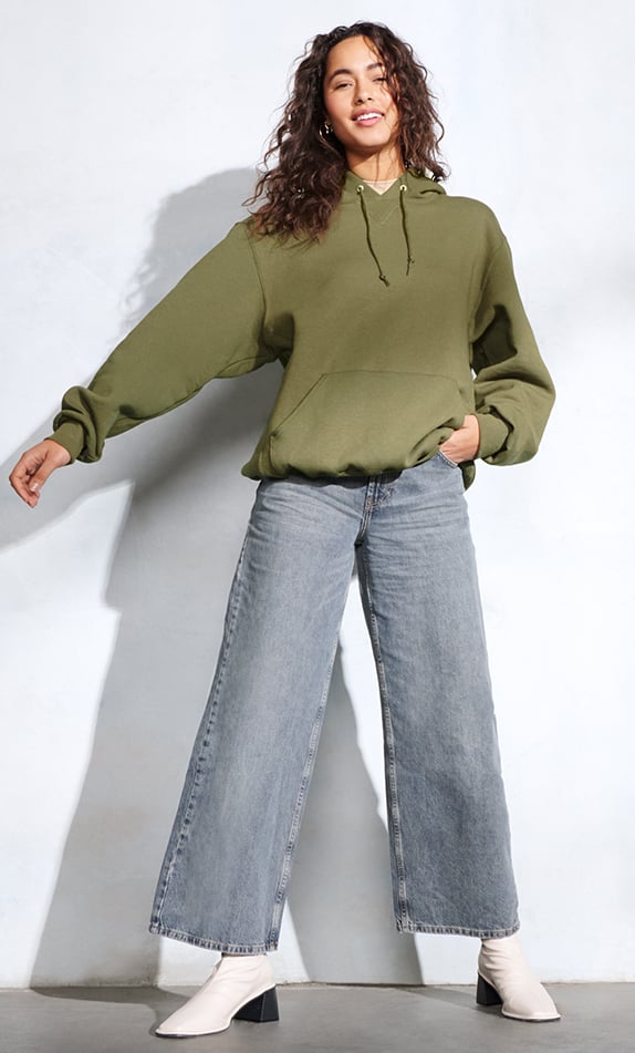 Female model wearing a green Russell Athletic Hoodie with Jeans and white boots. 