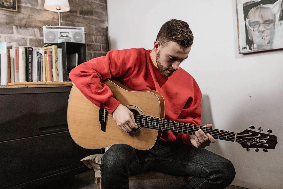 Man in Russell Athletic sweatshirt playing guitar.