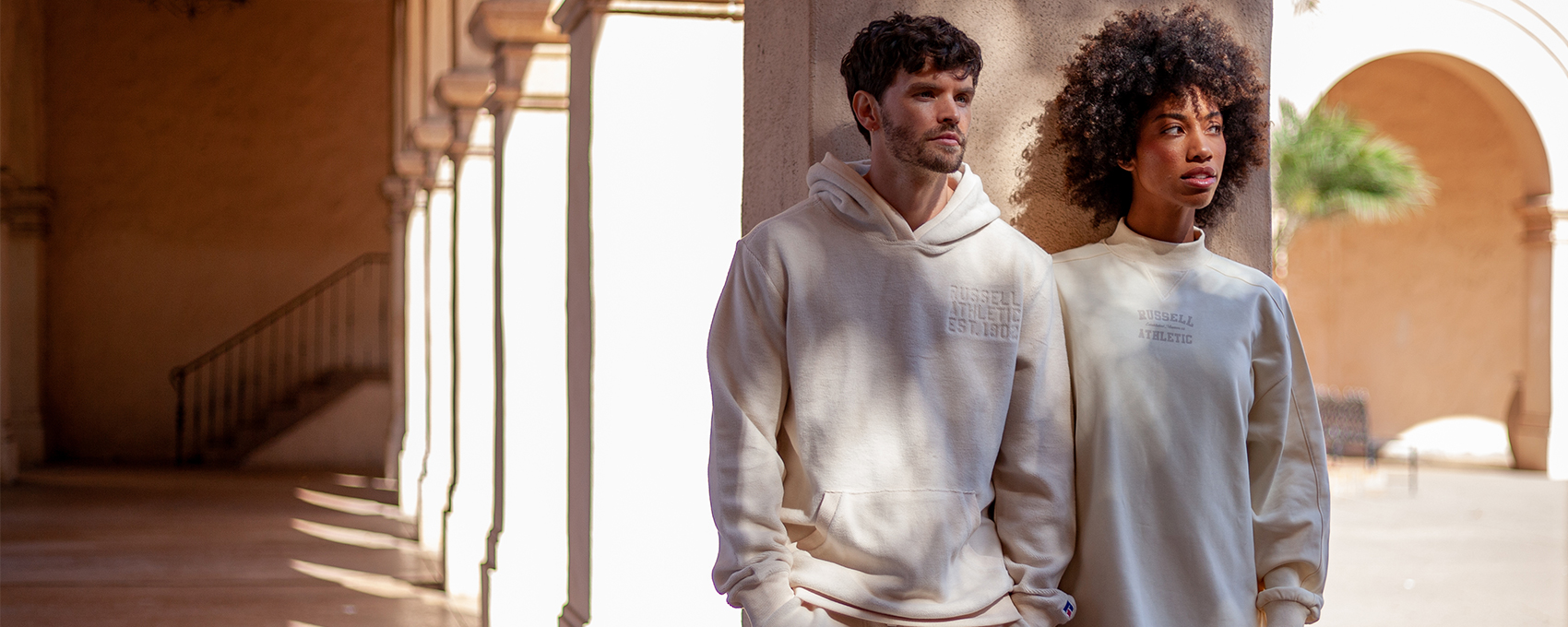 Male model in a cream hoodie and female model in a cream colored dress.