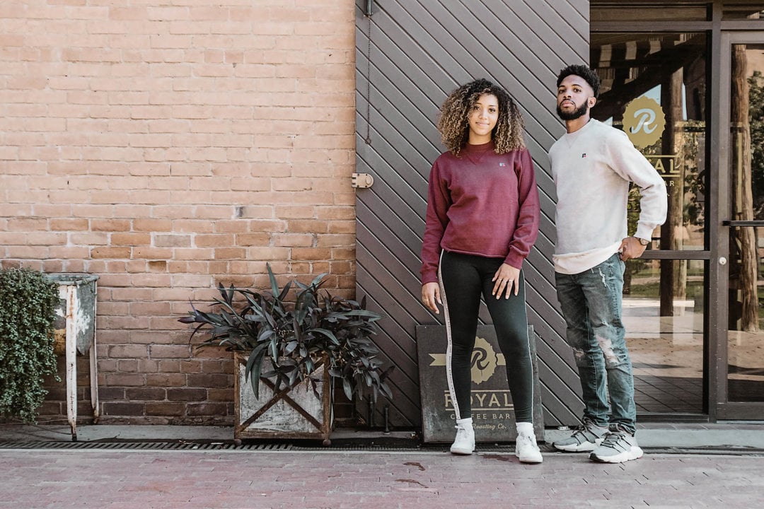 Man and woman posing in front of a building wearing Russell Athletic sweatshirts.