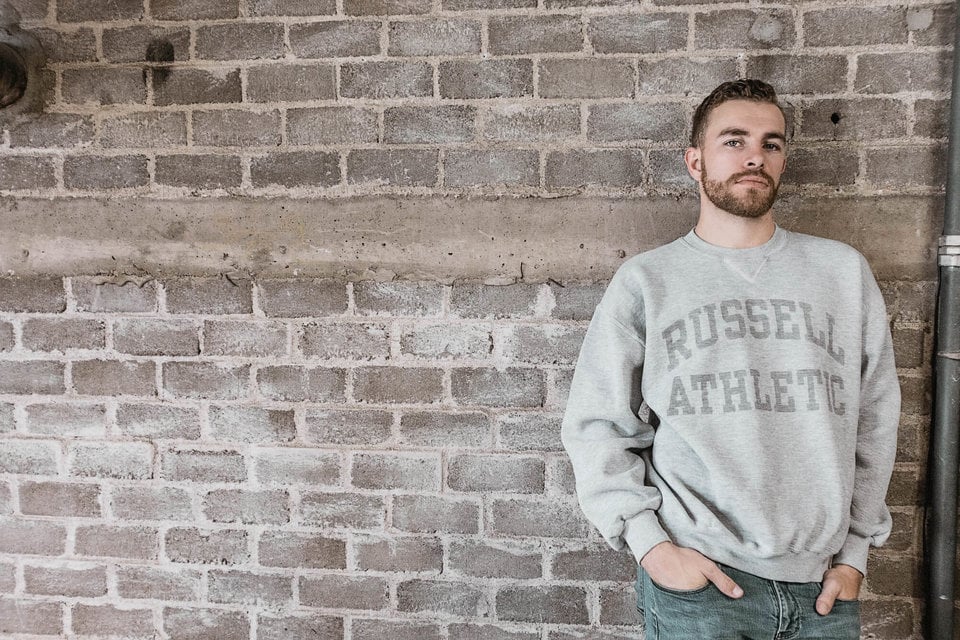 Man in Russell Athletic sweatshirt leaning on a brick wall.