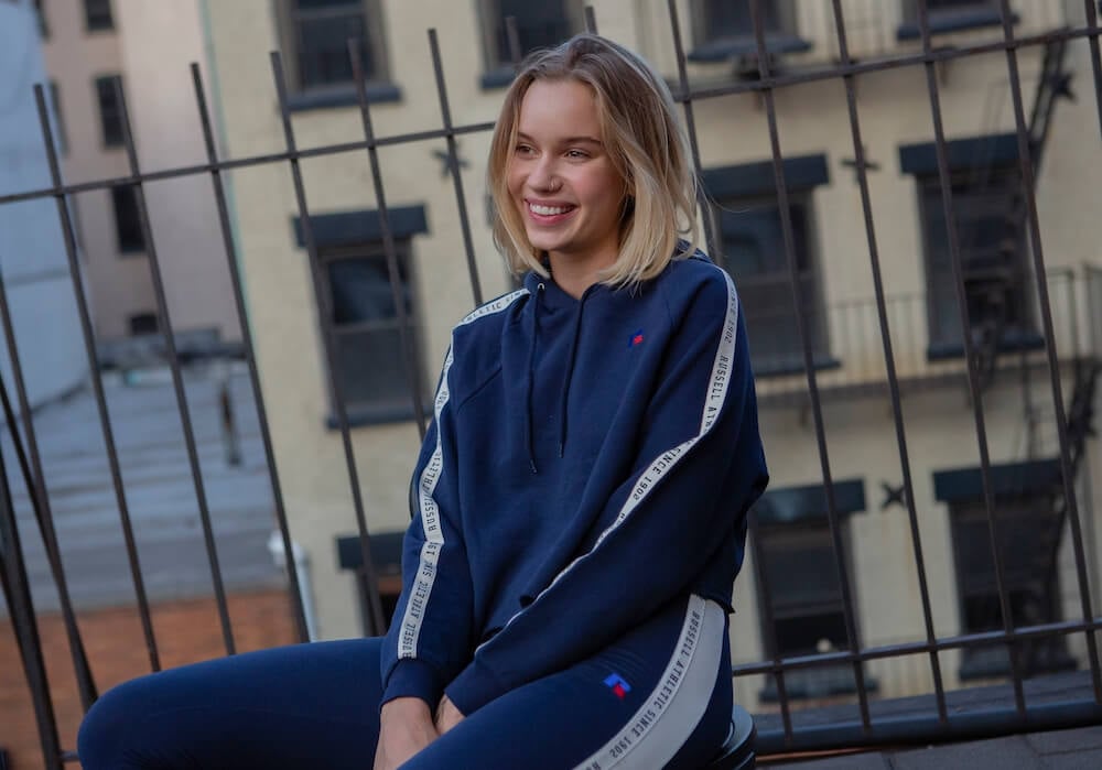 Woman sitting wearing a Russell Athletic sweatshirt and joggers.