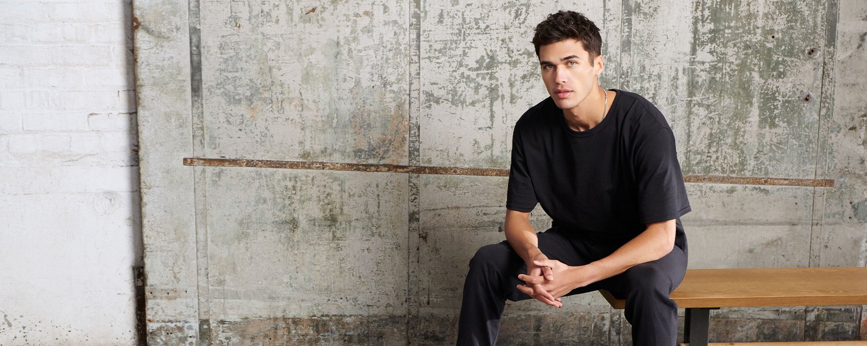 Male model sitting on a bench with black Russell Athletic tee.  